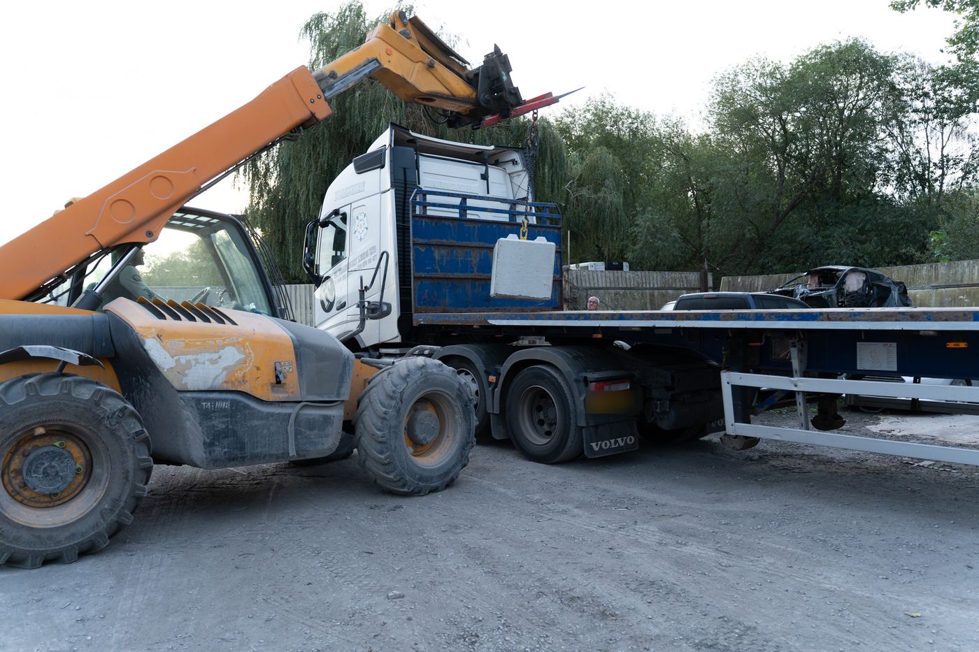 Telehandler lifting an interlocking concrete block onto a flatbed trailer